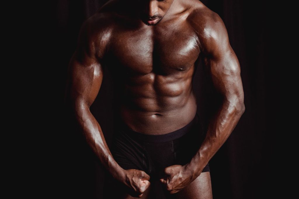 Athletic male bodybuilder flexing muscles in a dramatic studio setting, showcasing strength and physique.