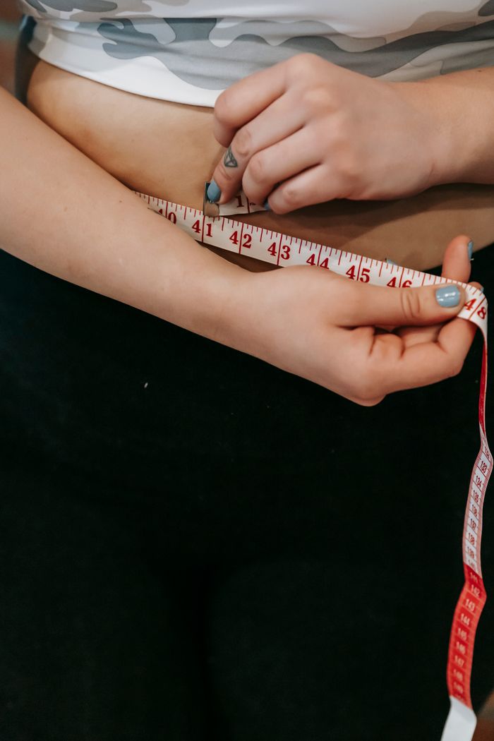 High angle of crop faceless overweight female measuring waist with centimeter for weight loss